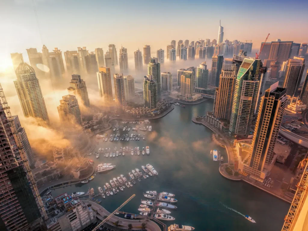 Aerial view of Dubai Marina harbour with yachts and luxury residential towers at sunrise.
